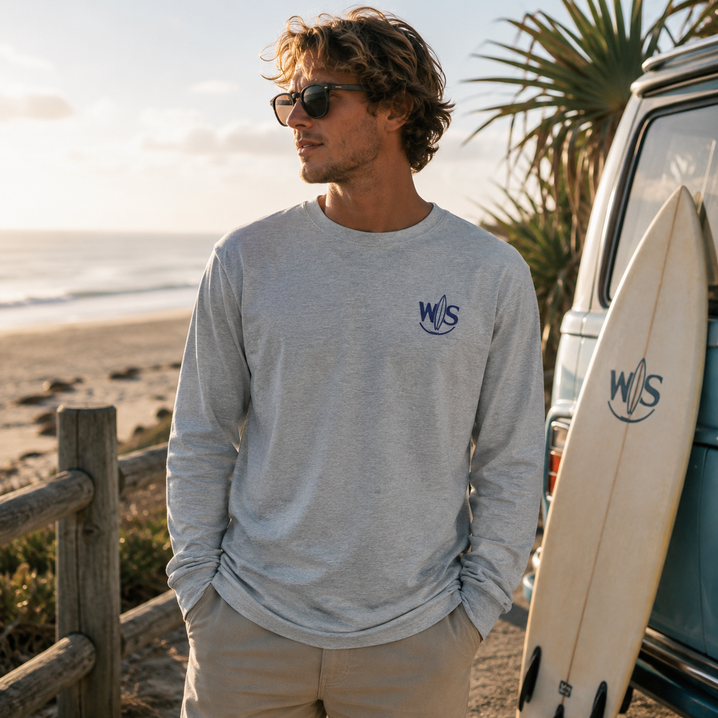 Man wearing a WaveSurfing™ grey heavyweight long sleeve T-shirt with WS surf logo in a coastal beach setting at sunset.