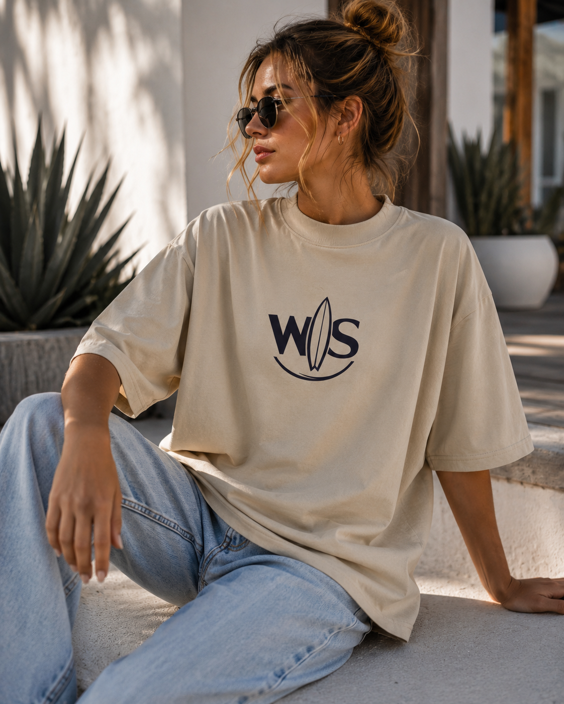 Young woman wearing the WaveSurfing™ Unisex Organic Oversized High Neck T-Shirt in a relaxed outdoor setting, featuring the minimalist WS surfboard logo and premium coastal streetwear style